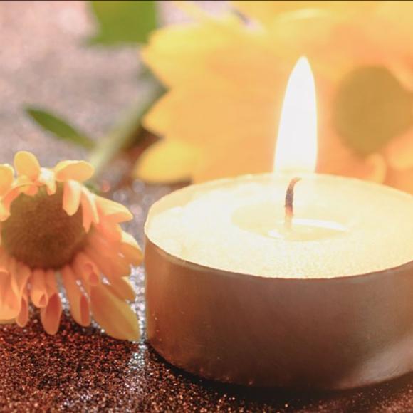 Lit tealight candle surrounded by yellow daisy flowers. Warm light.