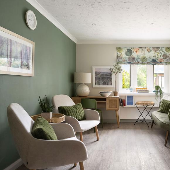 Stylish room with a green accent wall, two armchairs, floral window blind, and white storage cabinet.