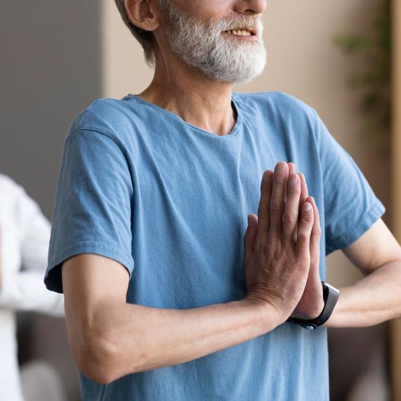 Elderly couple meditating, hands in prayer pose, serene expressions.