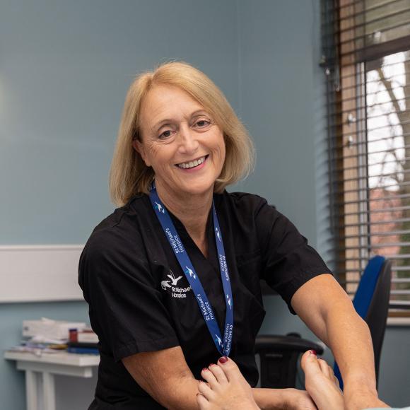 Smiling female healthcare professional examining a patient's foot in a clinic.
