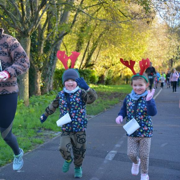 Smiling woman and two children in reindeer antlers running outdoors on a sunny day.