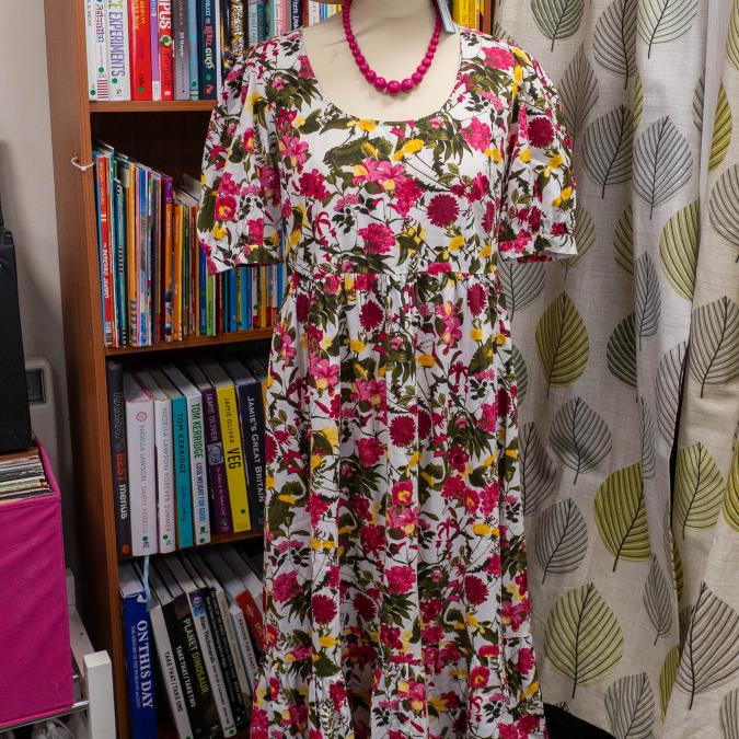 Mannequin wears a white floral midi dress, straw hat, chunky pink necklace, and pink sandals.