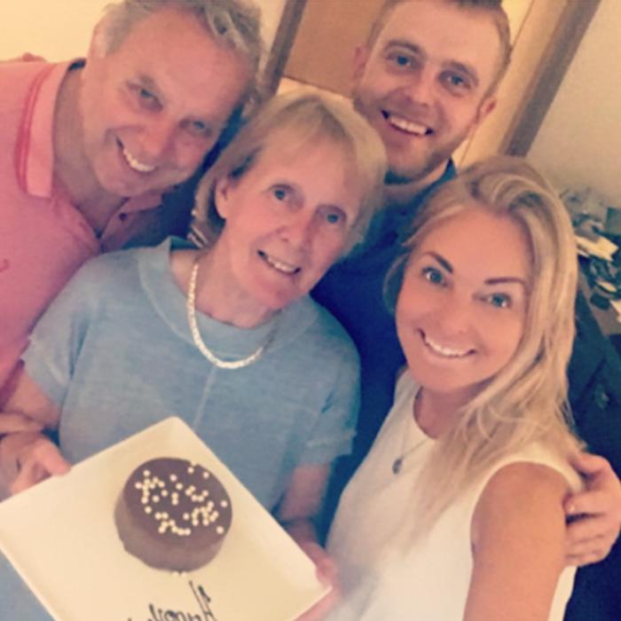 Smiling family of four holds a small chocolate cake with sprinkles.