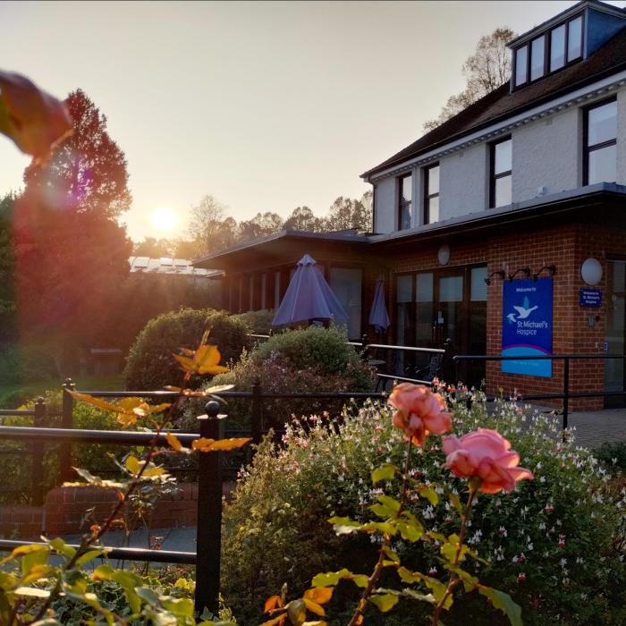 Warm sunset lights a building with an outdoor patio, garden, and prominent pink roses.