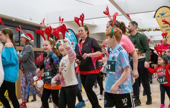 Adults and children in Christmas outfits, some with reindeer antlers, at a festive indoor event.