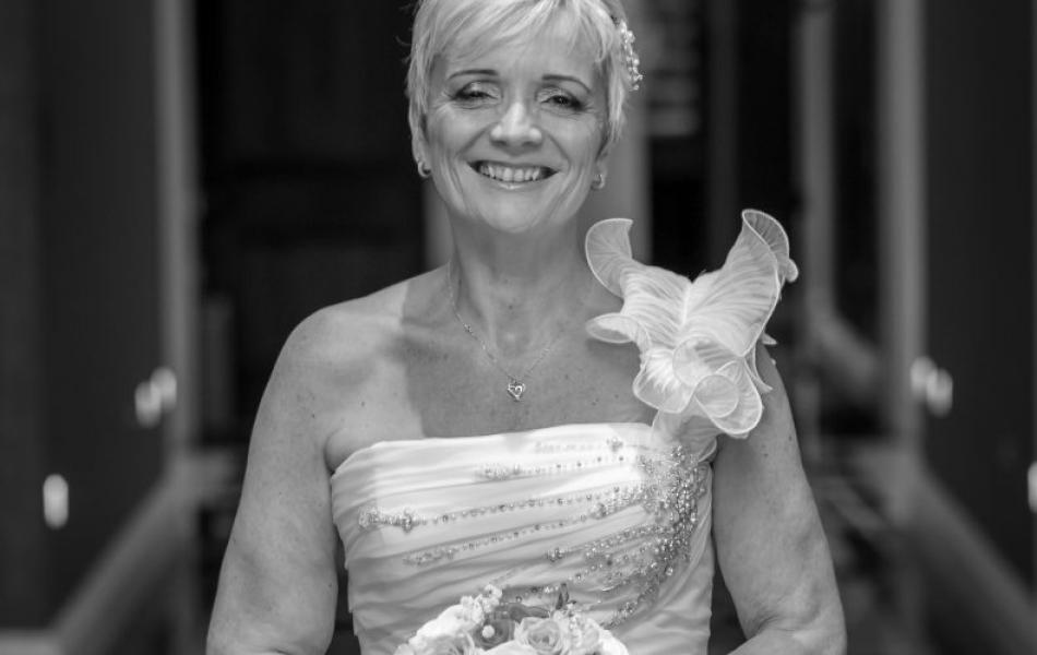Smiling woman in a wedding dress holding a bouquet in a hallway.