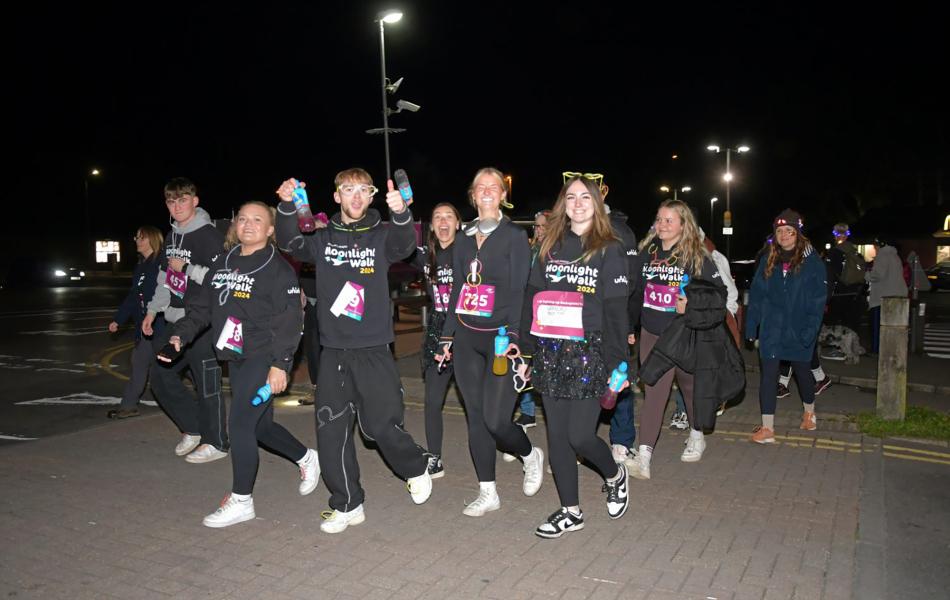 Young people in black activewear with glow sticks walking at night.