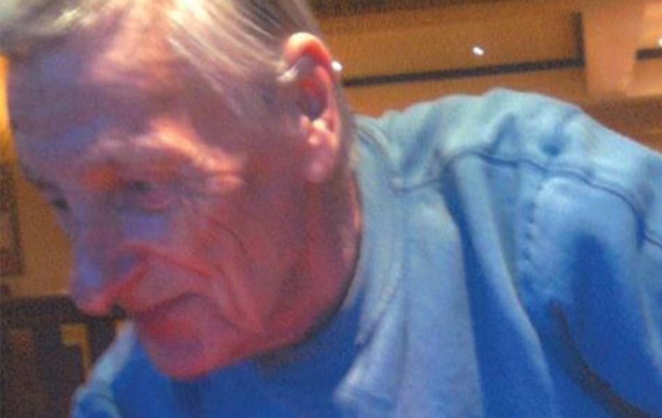 Older man with gray hair wearing a blue shirt, looking down.