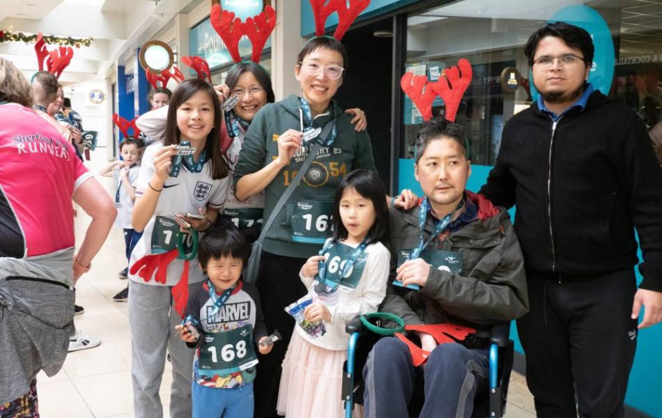 Festive group with reindeer antlers and race bibs, one adult in a wheelchair, in a mall.