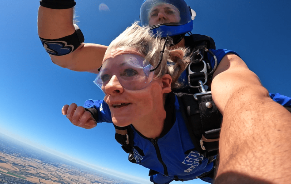 Smiling woman and instructor skydiving in blue suits against a clear blue sky.