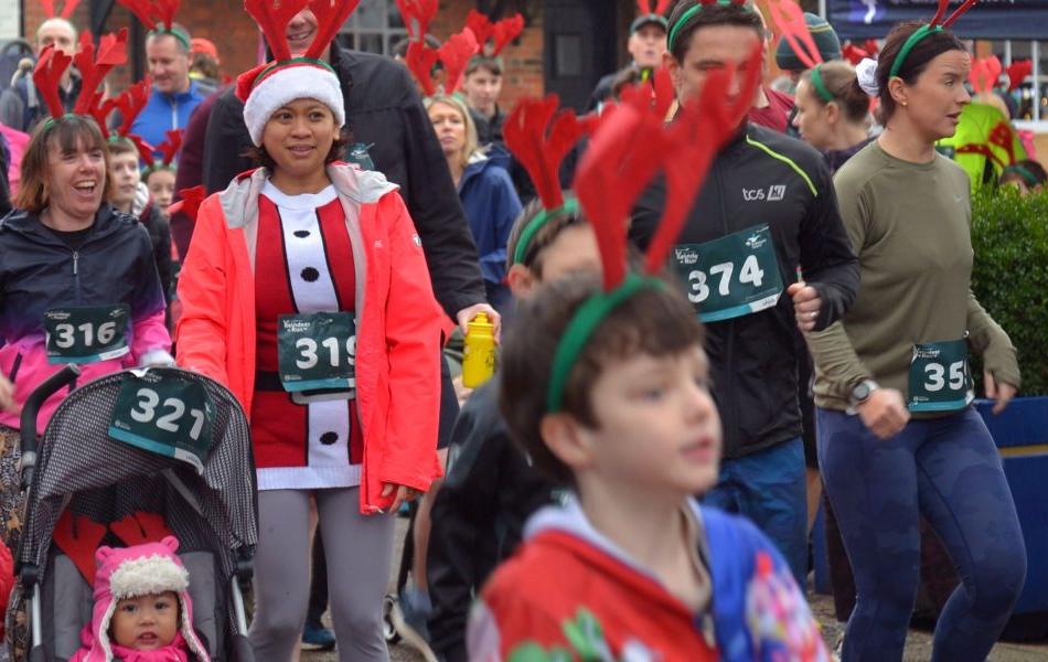 Runners of all ages in festive Christmas attire and race bibs participate in a holiday fun run.