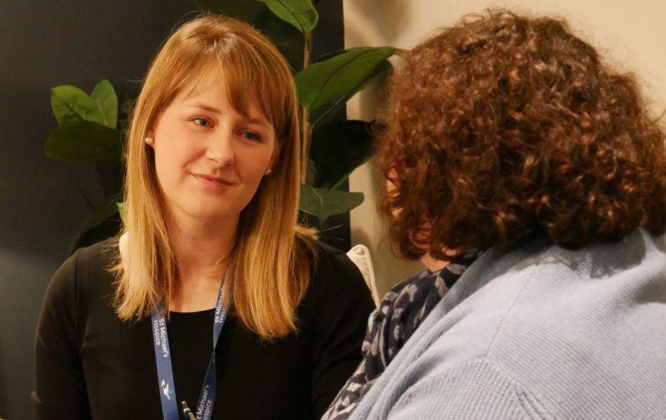 Young woman with blonde hair and lanyard listens to another woman.