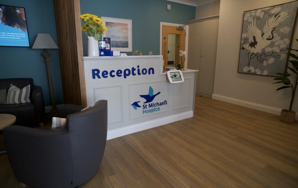 Bright hospice reception with "Reception" desk, armchairs, and art.