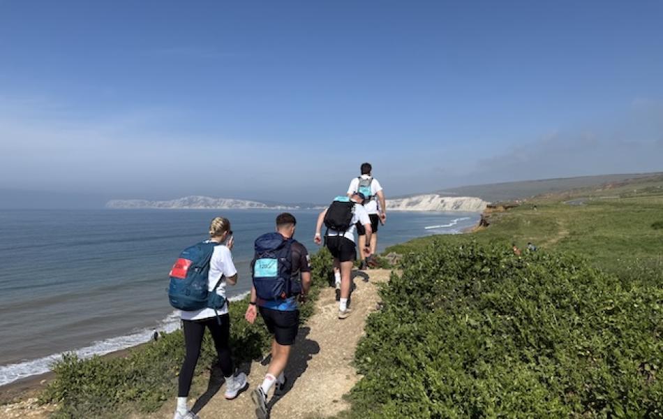 People walking away from the camera on a coastal path the the blue sky and sea scene in the background