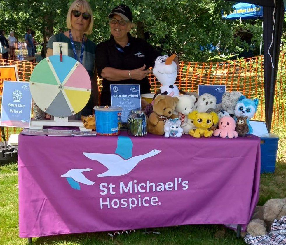 St Michael's Hospice stand at an outdoor event, with two women, a prize wheel, and toys.