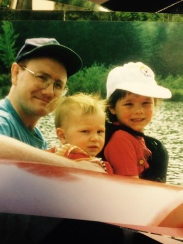 Smiling man and two young children in a boat on the water.
