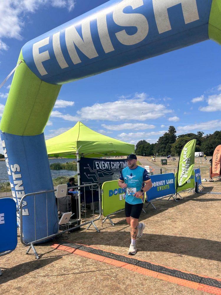 Man running under a blue "FINISH" arch at an outdoor race.