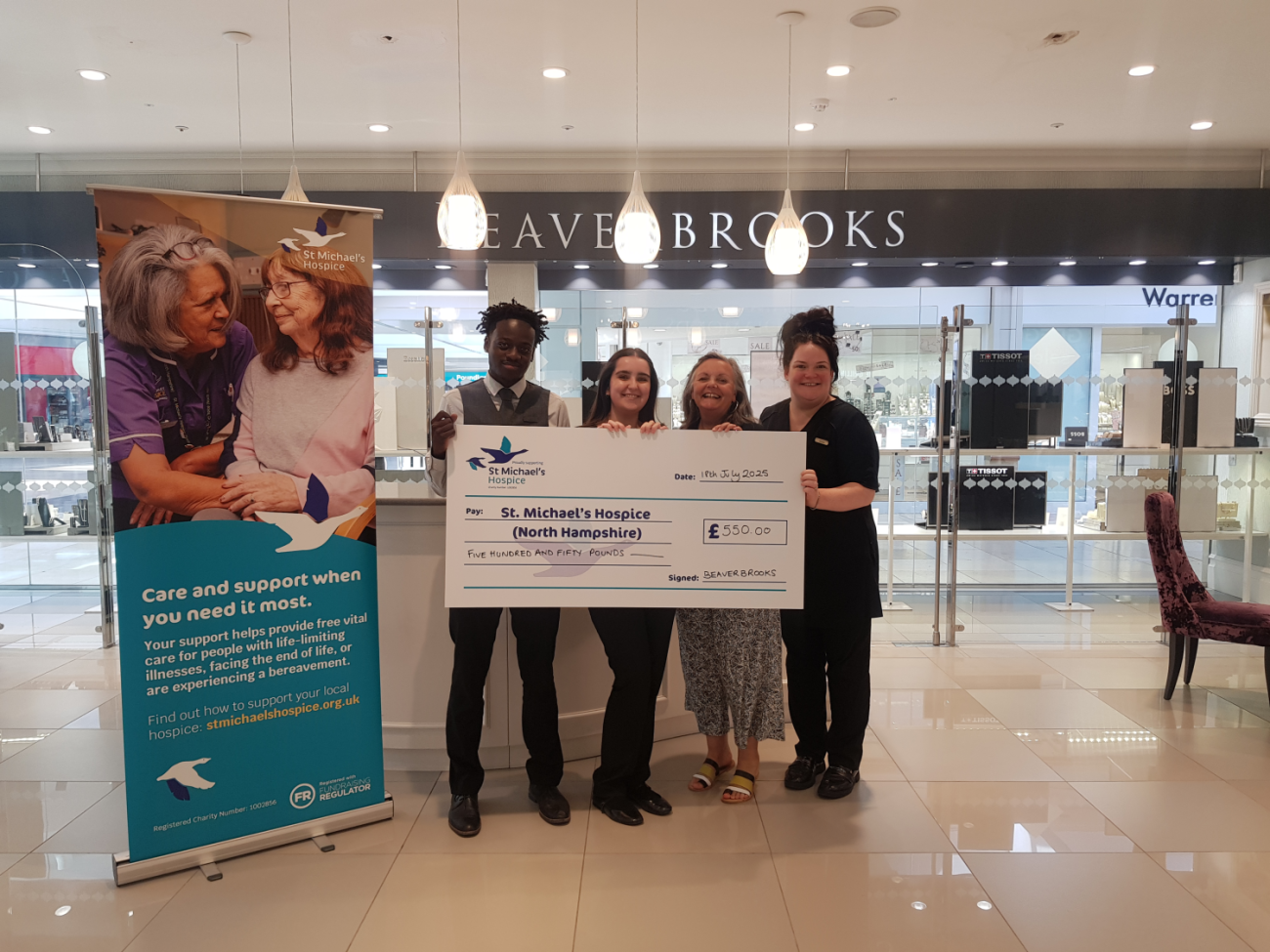 Four people smiling, presenting a large check for £1,029 to Blind Veterans UK.