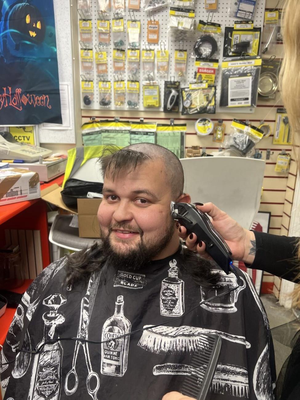 Smiling man with a half-shaved head gets a haircut with electric clippers.