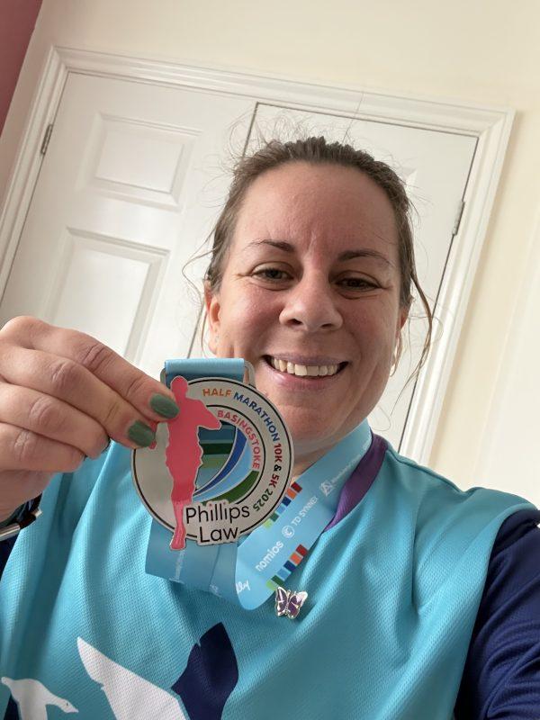Happy woman holds up a "Great North Run" marathon medal, smiling proudly.