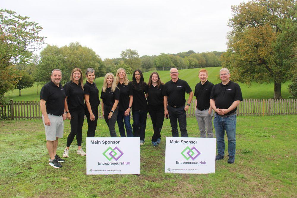 Ten people in black shirts with "Main Sponsor" signs and logo outdoors.