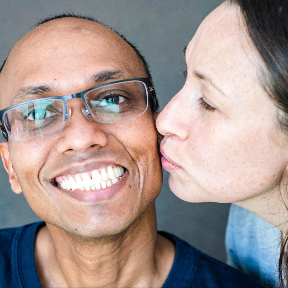 Woman kisses a smiling man's cheek.