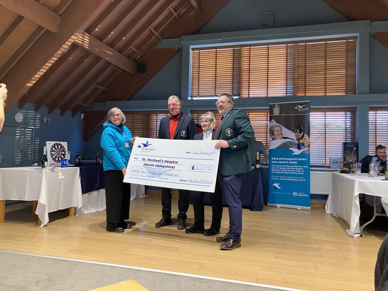 Four people, including a child, hold a large check for St Michael's Hospice on stage.