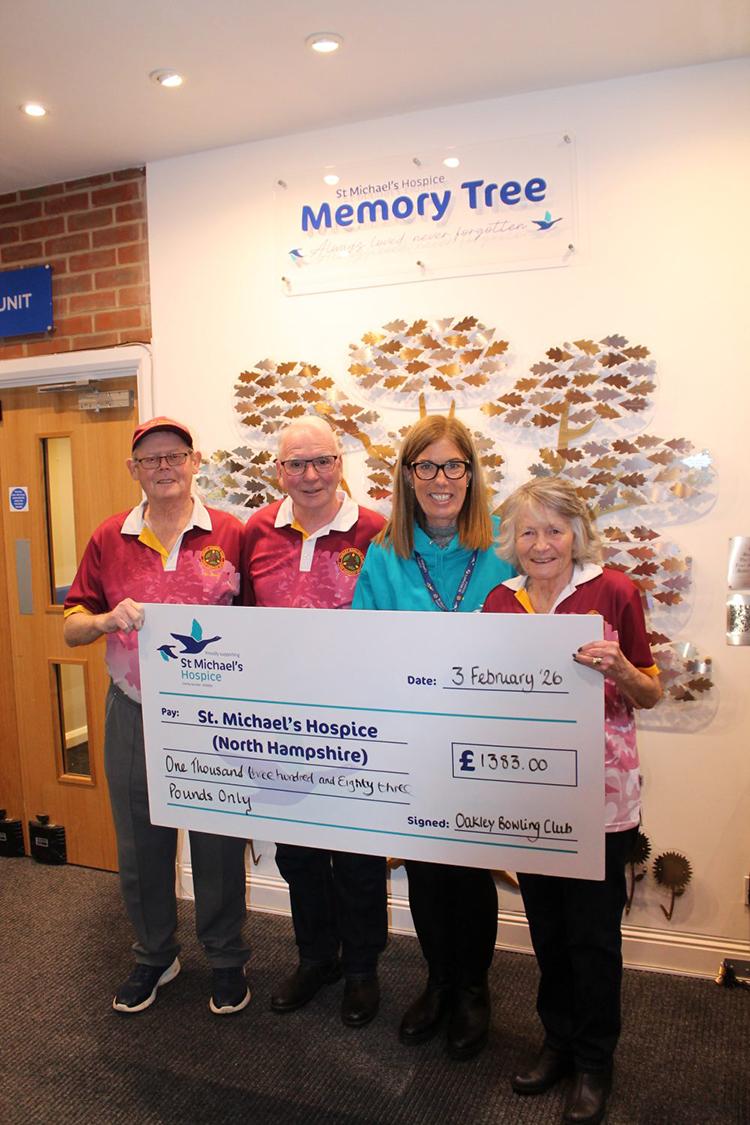 Group of four presents a £1743 check to St Michael's Hospice, with a Memory Tree behind them.