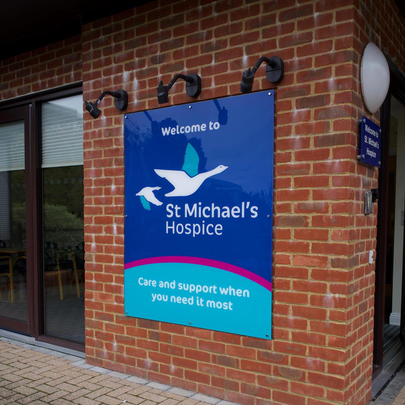 Sign for St Michael's Hospice on a brick wall, with a bird logo.