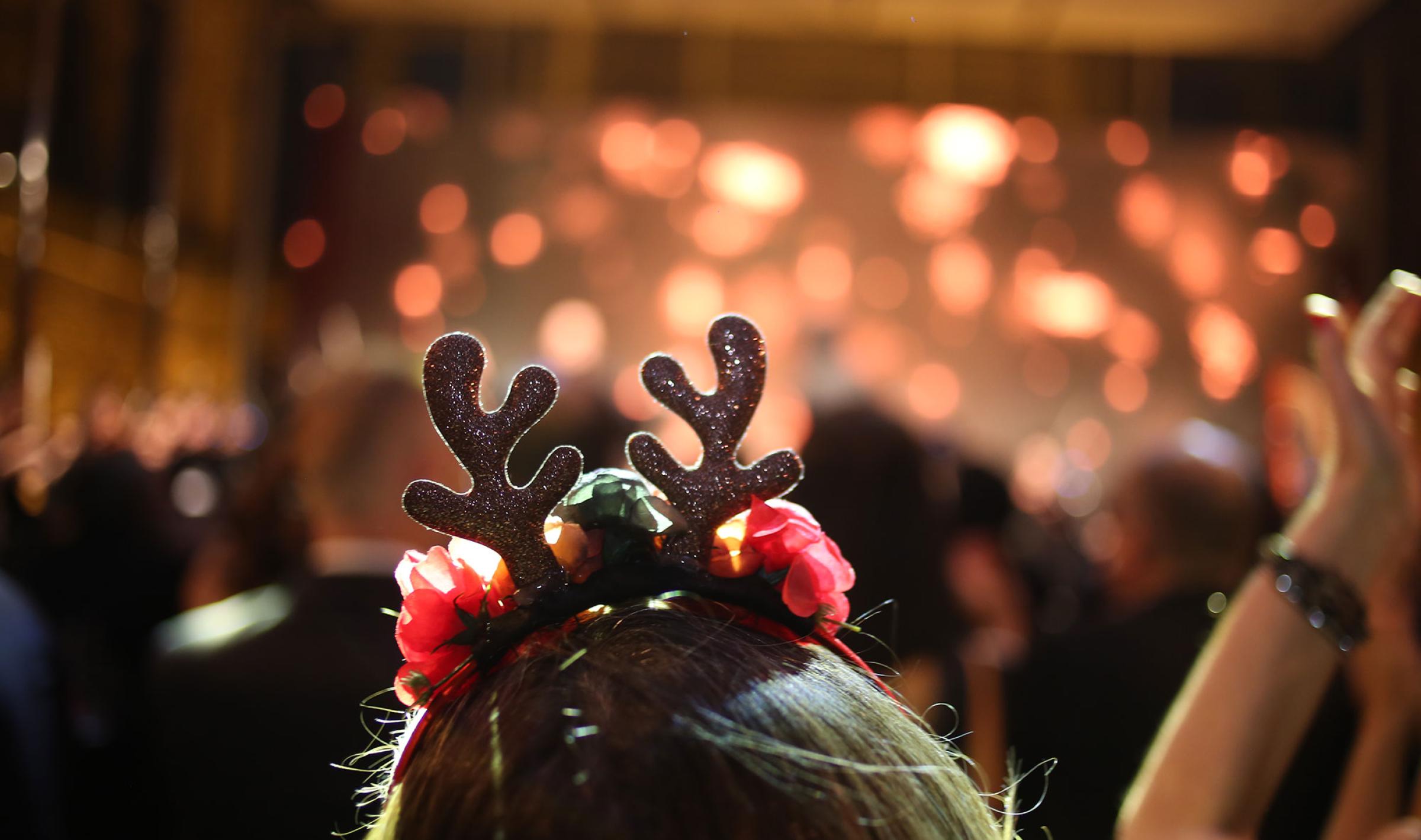 Back of a head with glittery reindeer antlers at a blurred, warmly lit party.
