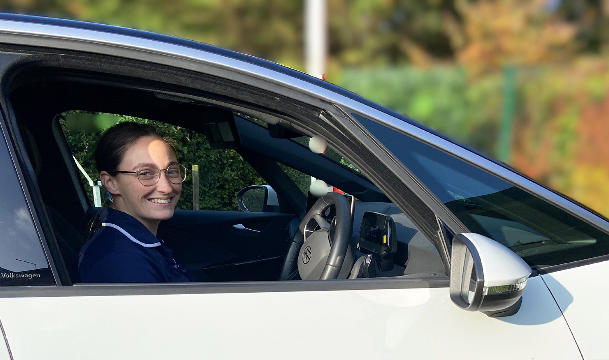 Happy healthcare worker in a white car displaying the St Michael's Hospice logo.