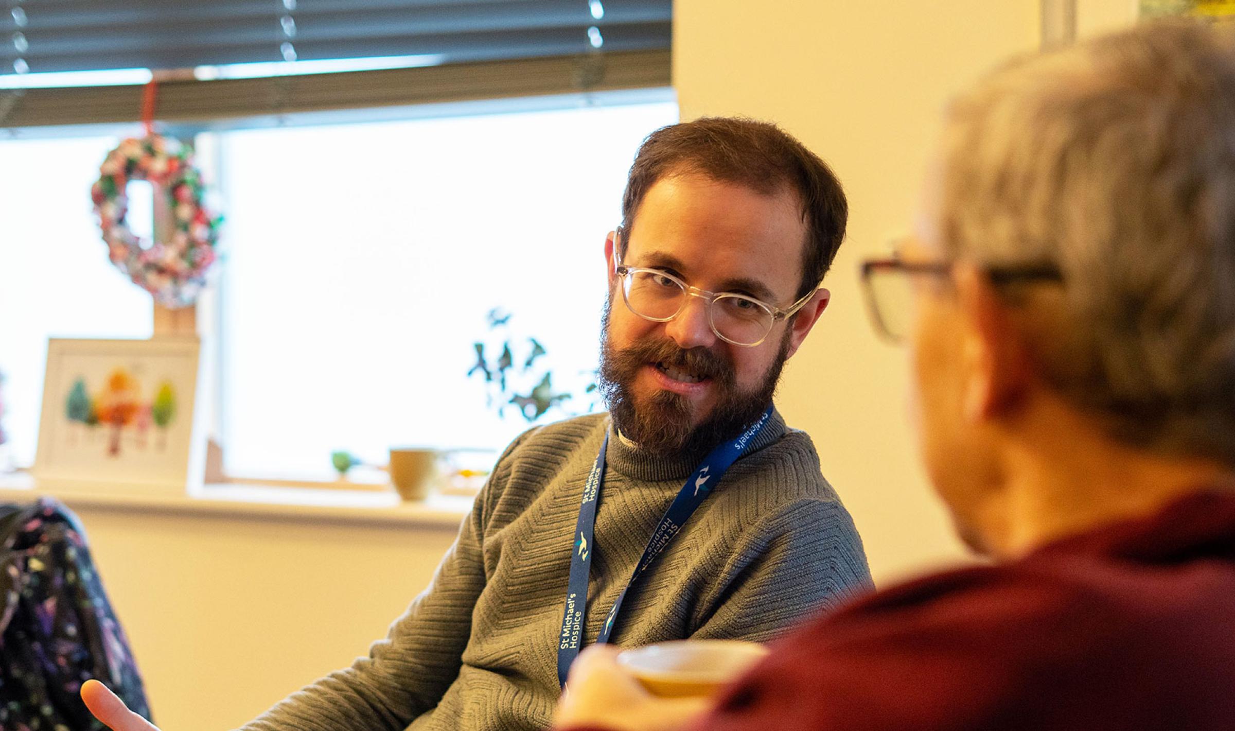 Photograph: Bearded man with glasses gestures, talking to another person.