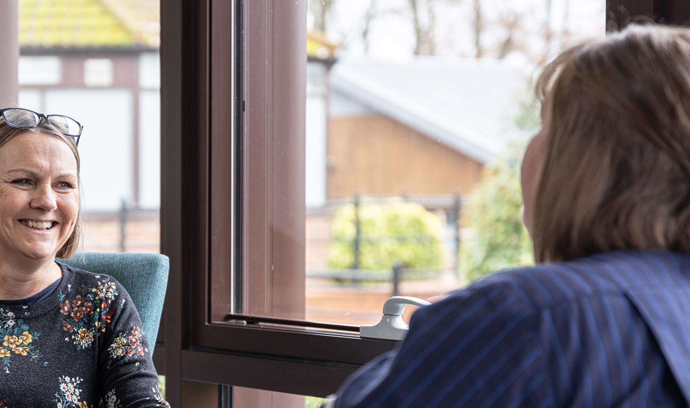 Two women talking indoors. One smiles at the other, who wears a uniform.