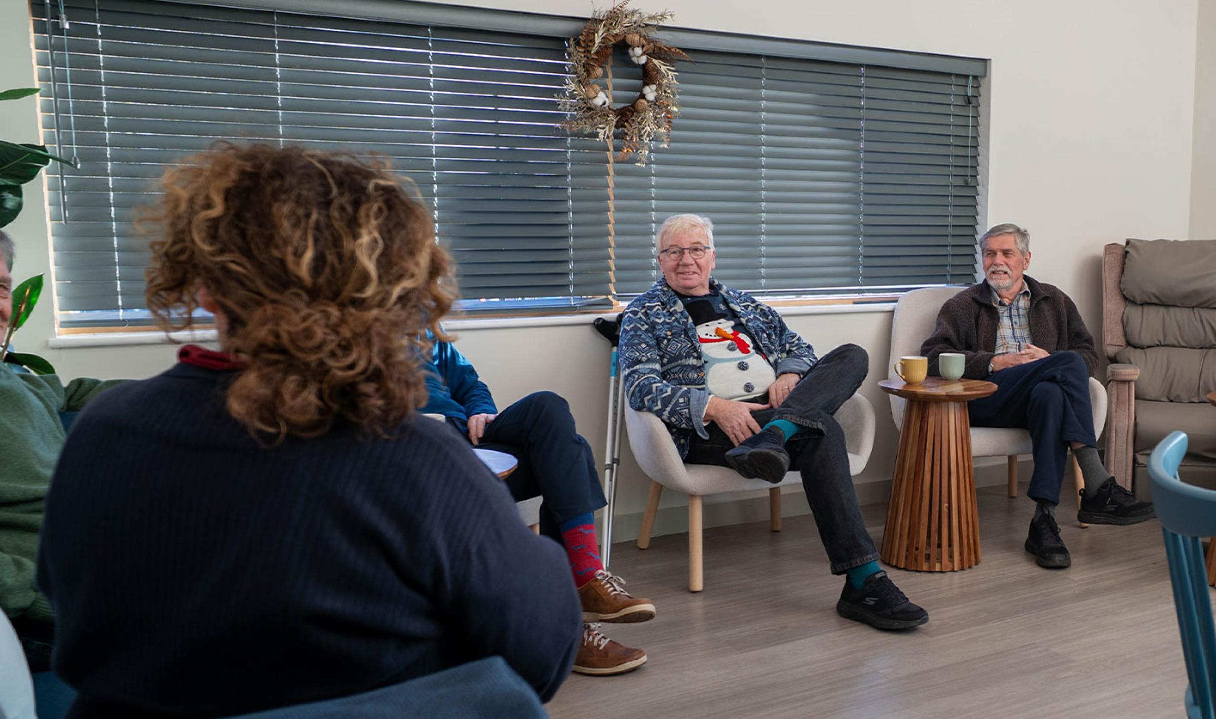 People socialise in a modern lounge, sitting in a circle with drinks.