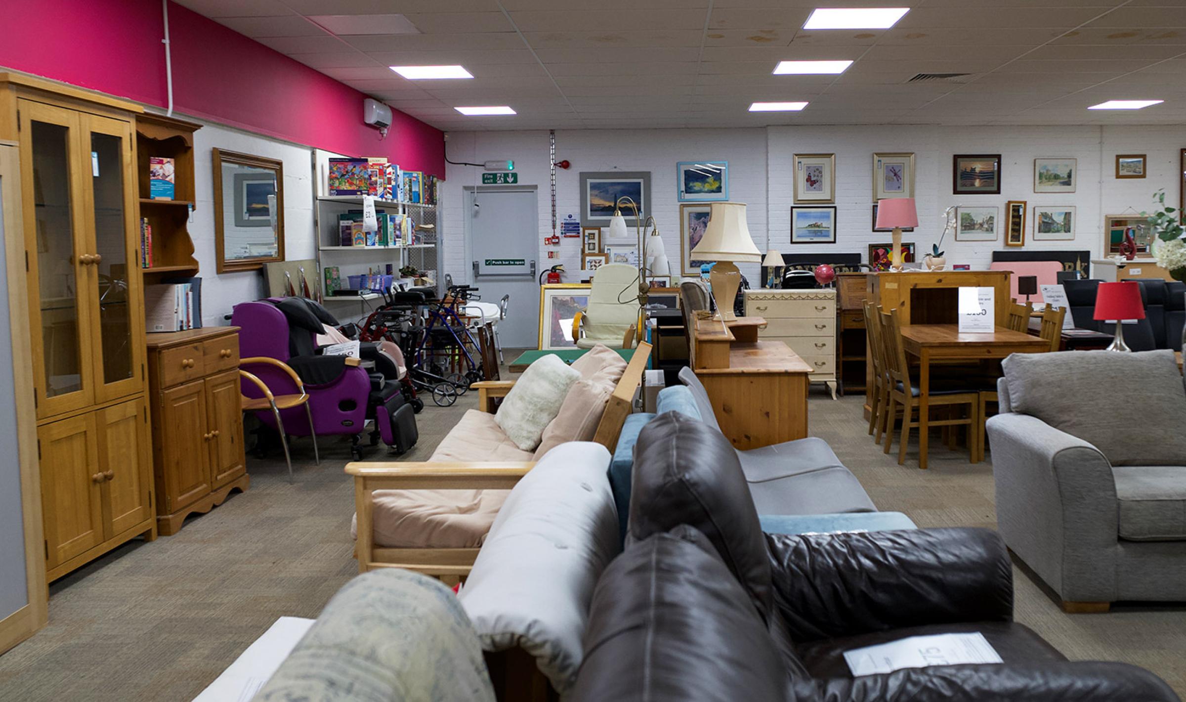 Charity shop interior with rows of assorted sofas, cabinets, and household furniture.