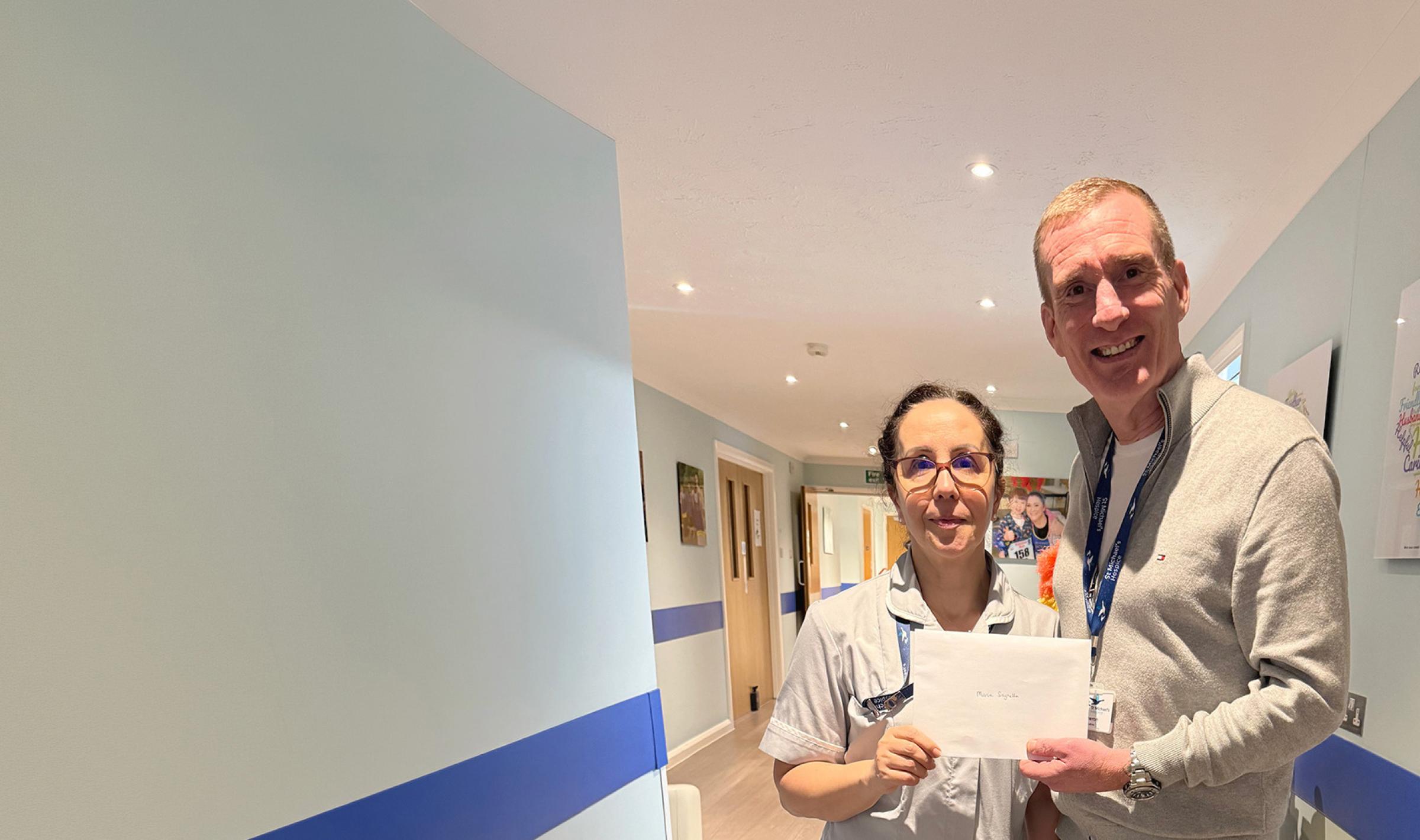 Man and nurse holding a white envelope in a light blue hallway.
