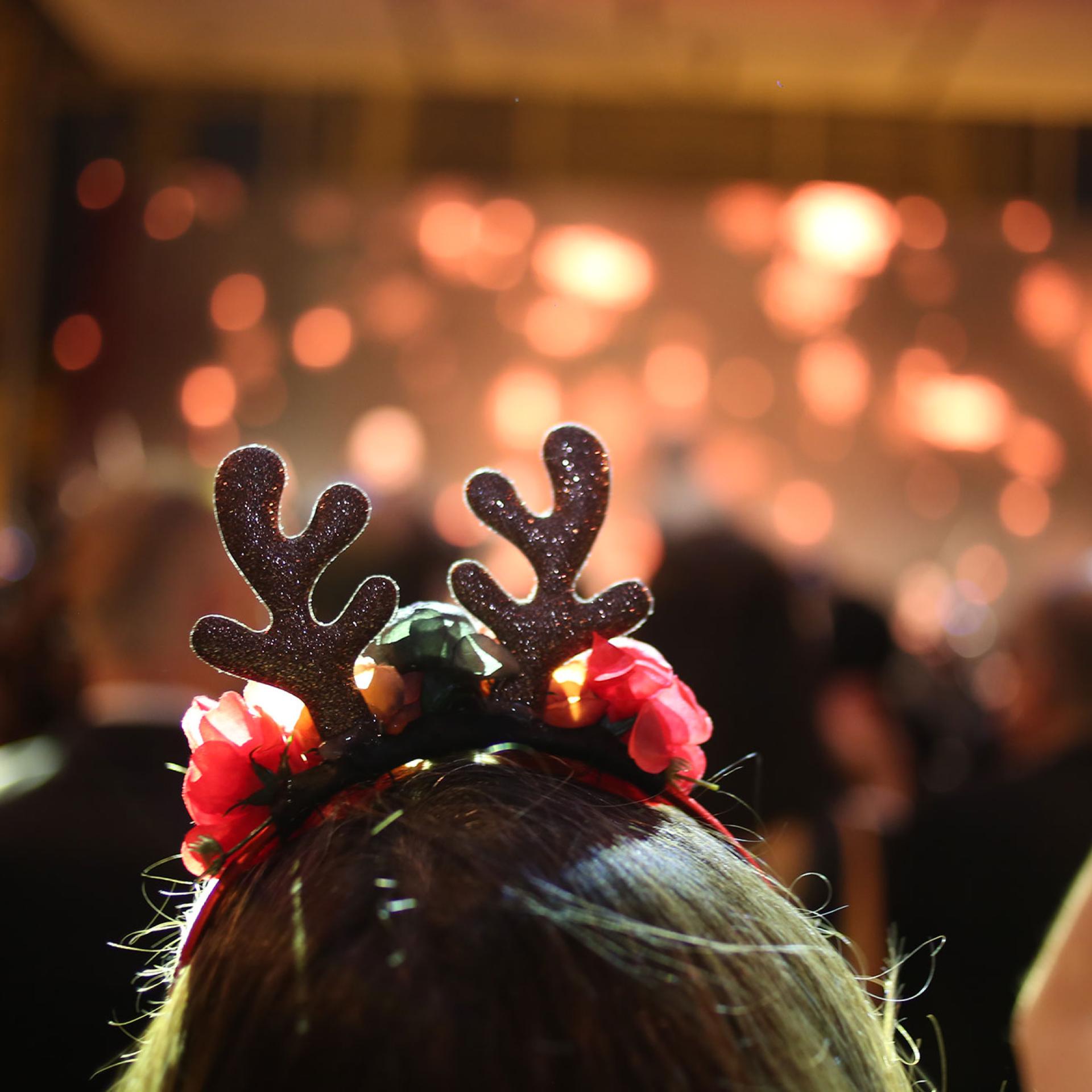 Person with glittery reindeer antlers at a festive party, soft bokeh lights.