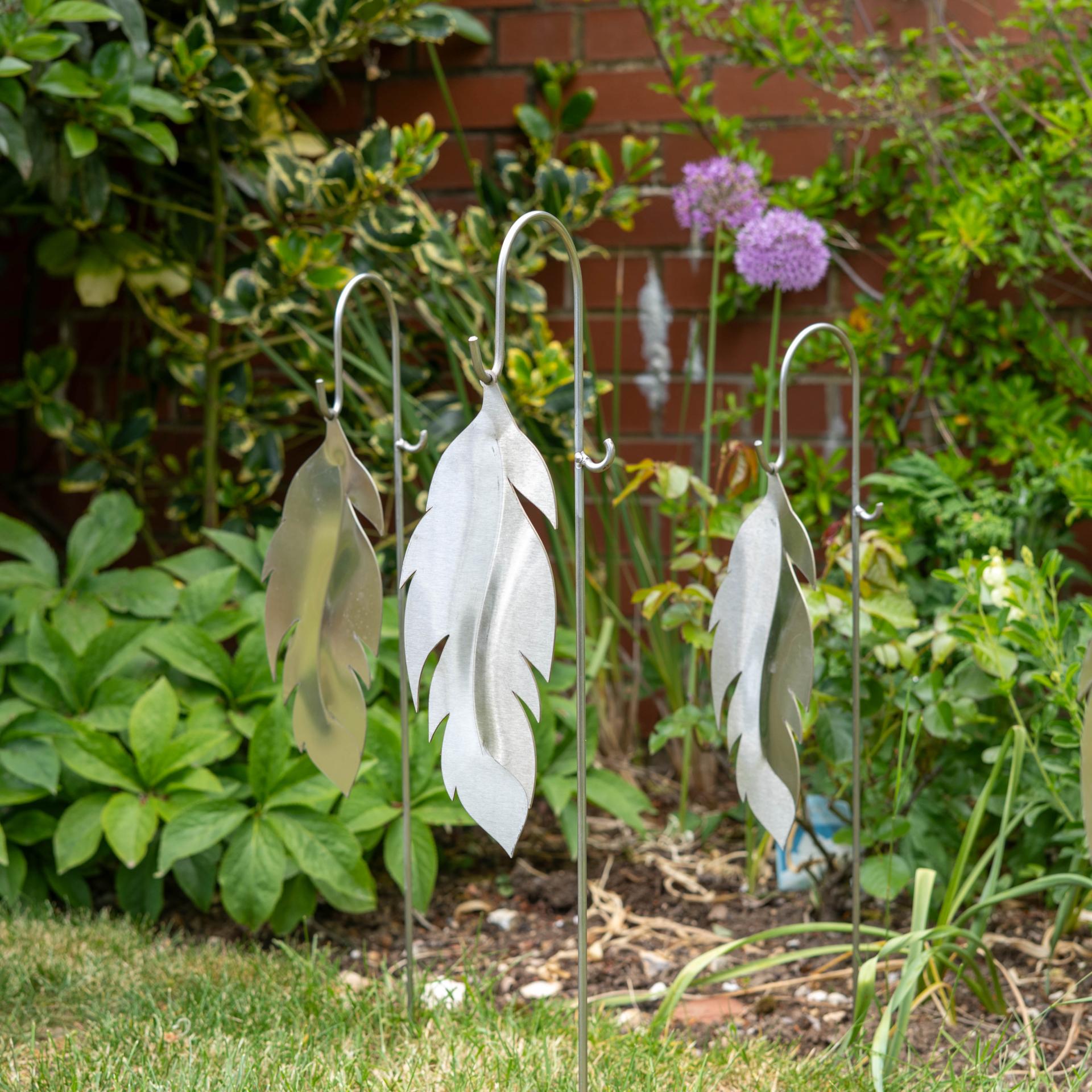 Metallic feather keepsakes hang in a sunny garden amongst green foliage and purple flowers.