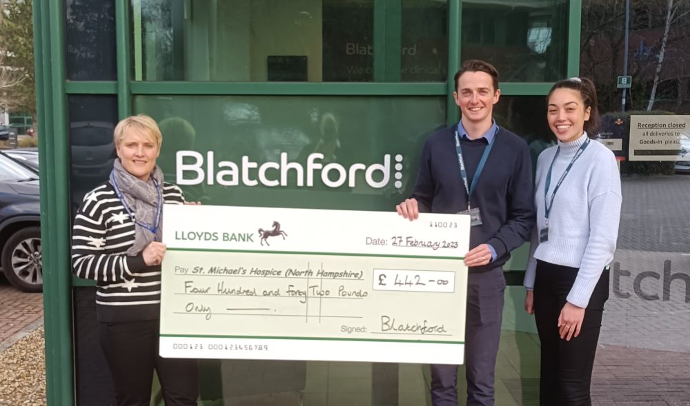 Three people holding a giant cheque smiling at the camera