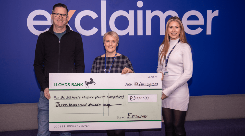 The people smiling at the camera holding a giant cheque by the exclaimer logo