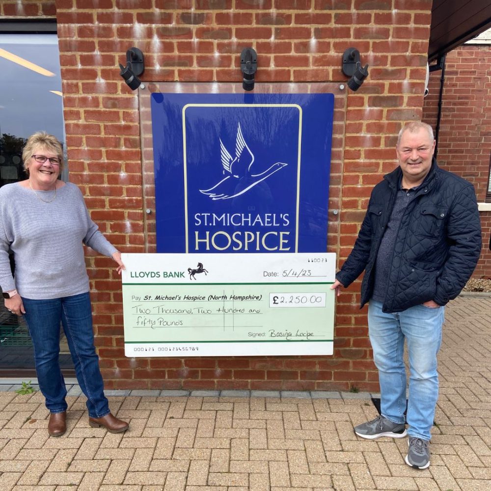 Image of two people holding a giant cheque outside ur Hospice