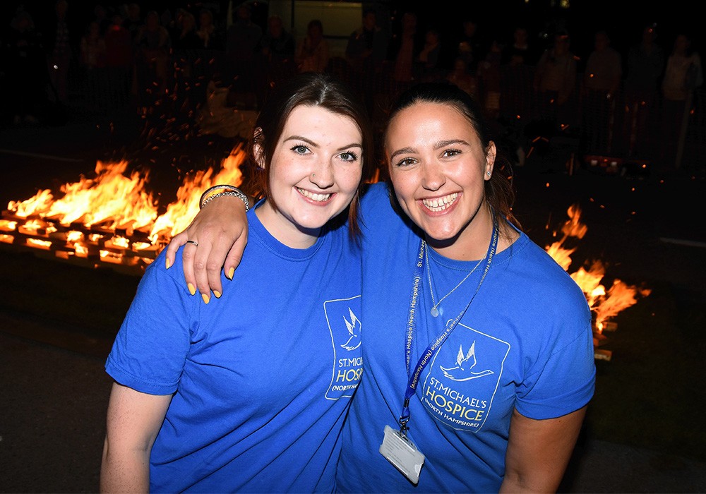 Two women smiling at the camera in front of a fire for the Firewalk