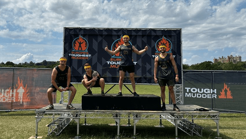 Four Tough Mudder participants stood on a podium after finishing their challenge