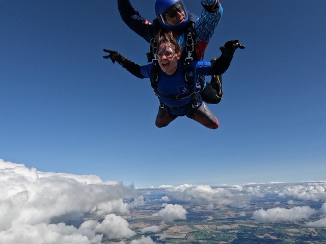 Image of supporter skydiving, with blue sky in background and clouds below