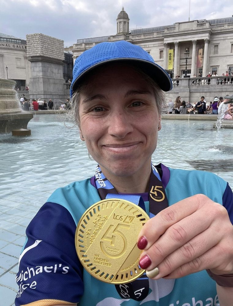 Lisa holding her medal after the London Marathon and smiling at the camera